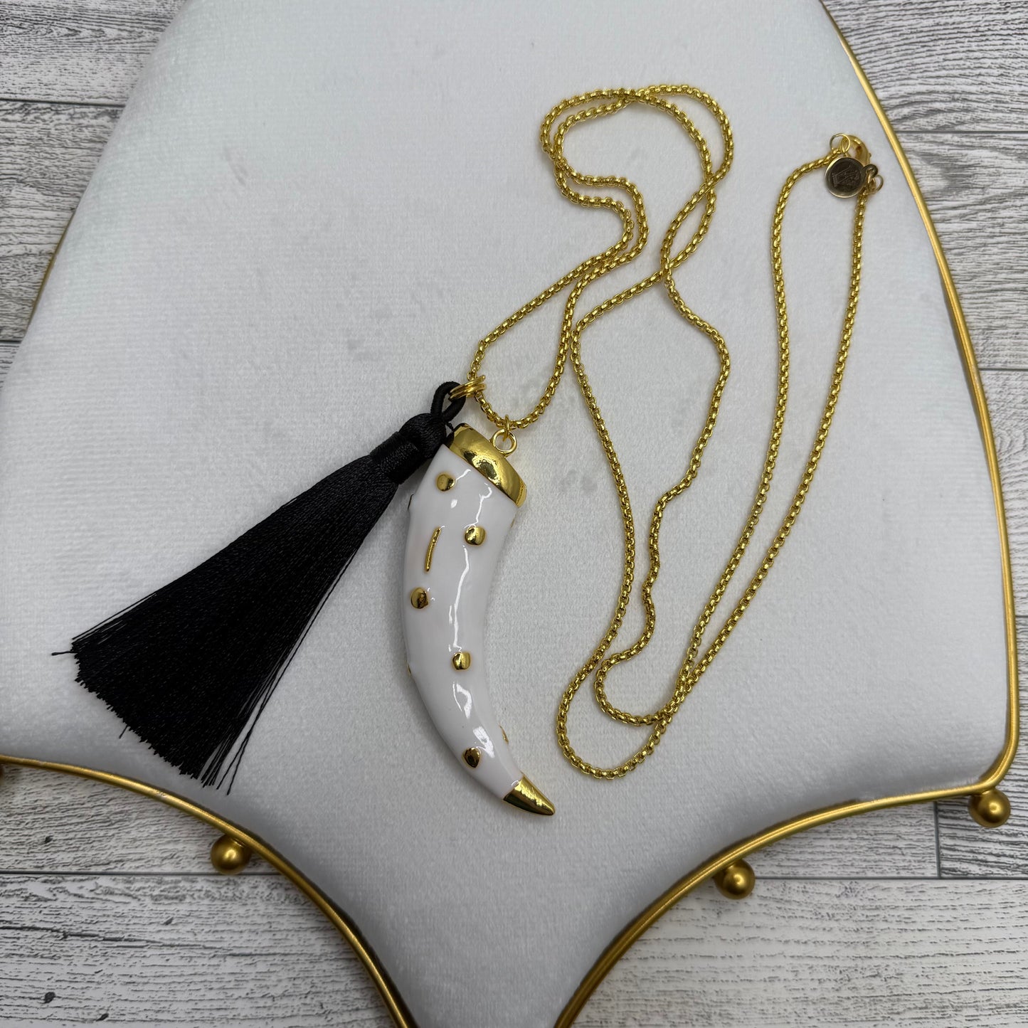 Gold necklace with a black tassel on a white cushion with gold trim