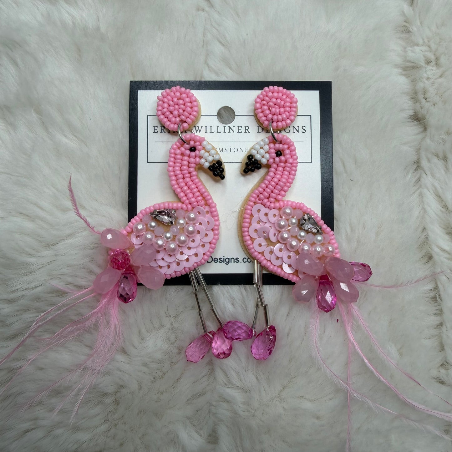 Pink beaded earrings on a branded card against a white fur background