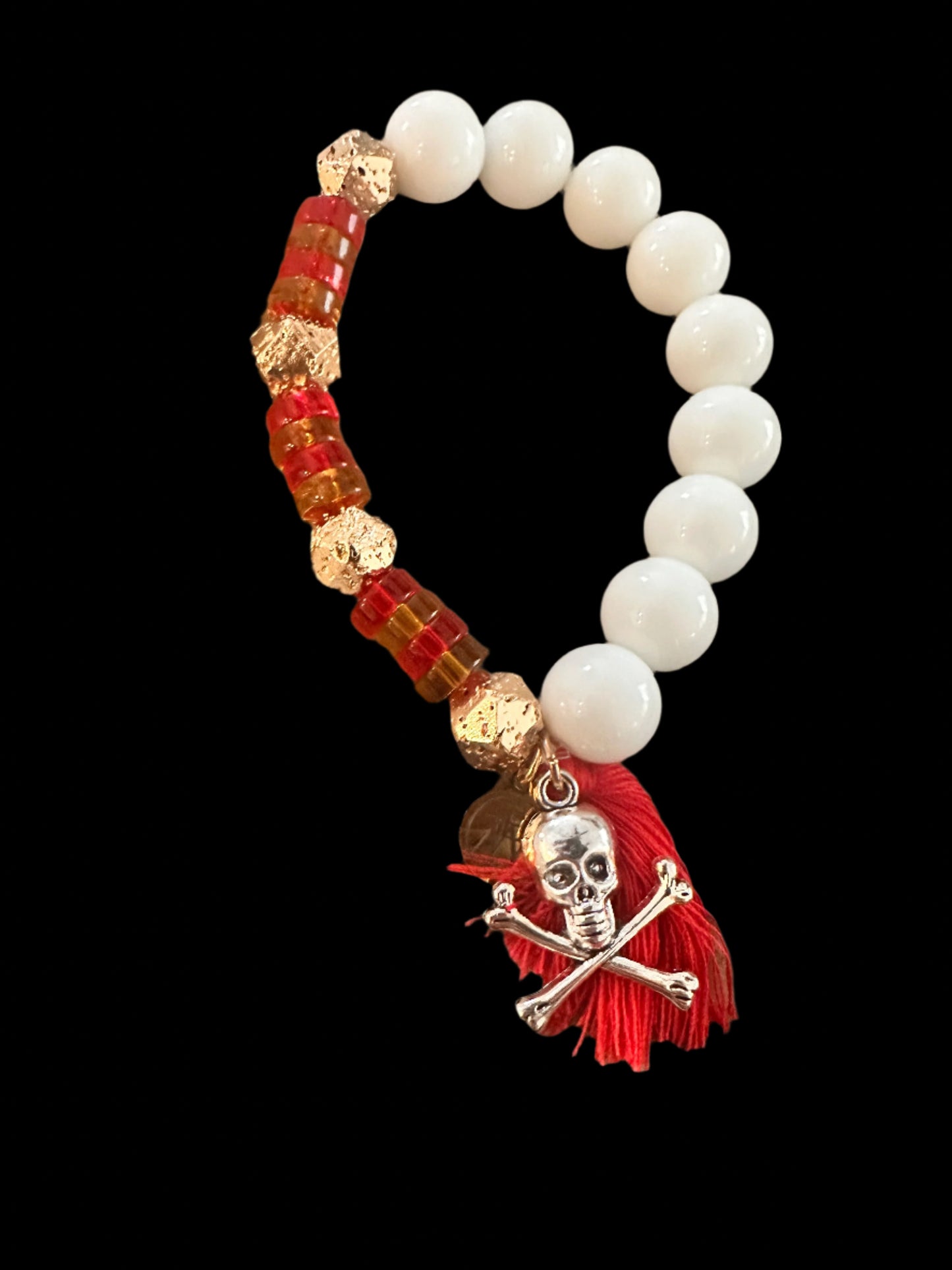 Bracelet with white beads, red and gold accents, and a skull charm on a textured surface.