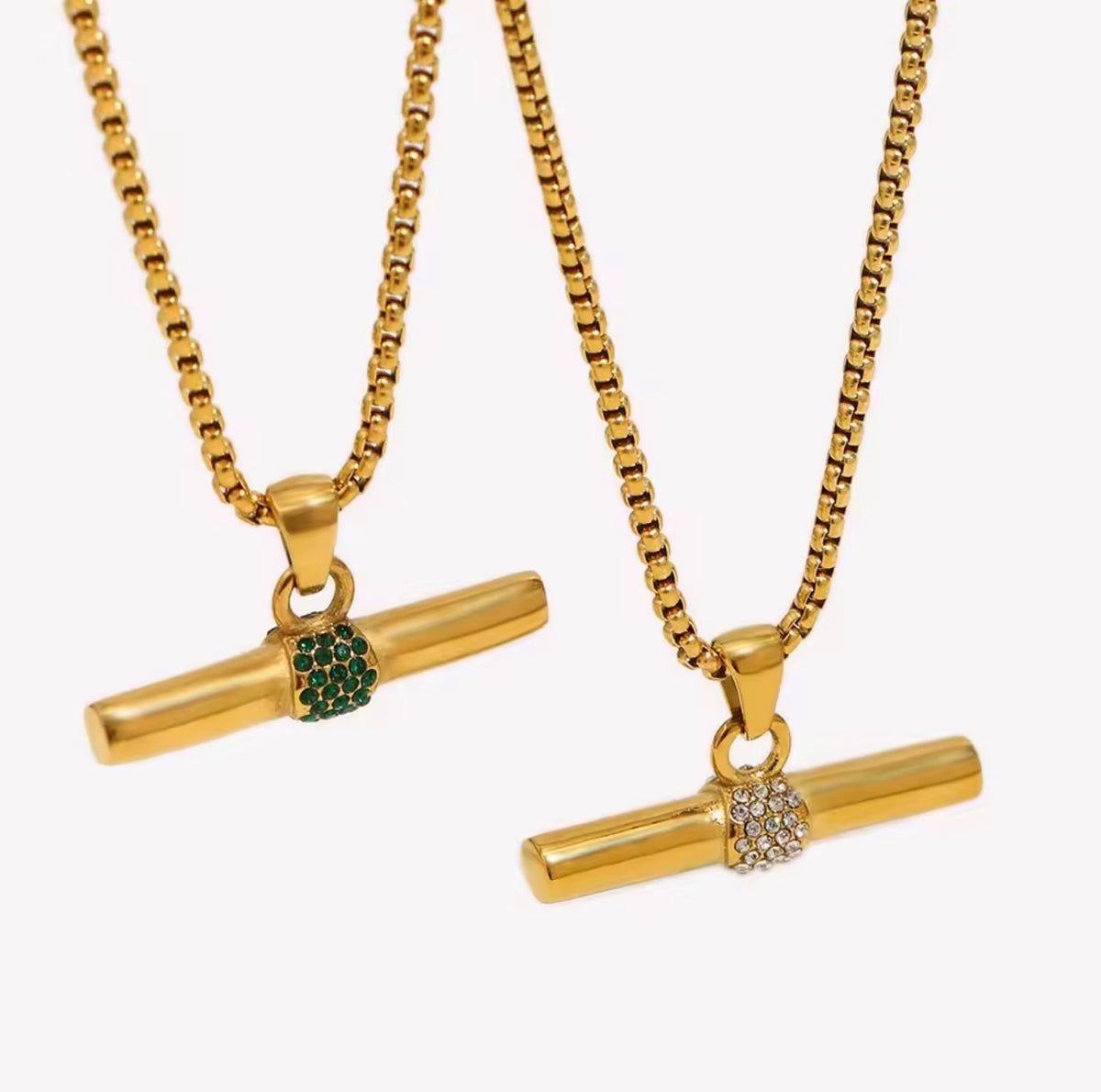 Two gold-tone box chain necklaces with horizontal bar pendants, each decorated with a small crystal-encrusted round accent. One accent is green, and the other is clear, shown against a plain light gray background.