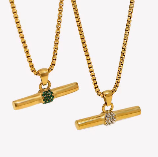 Two gold-tone box chain necklaces with horizontal bar pendants, each decorated with a small crystal-encrusted round accent. One accent is green, and the other is clear, shown against a plain light gray background.