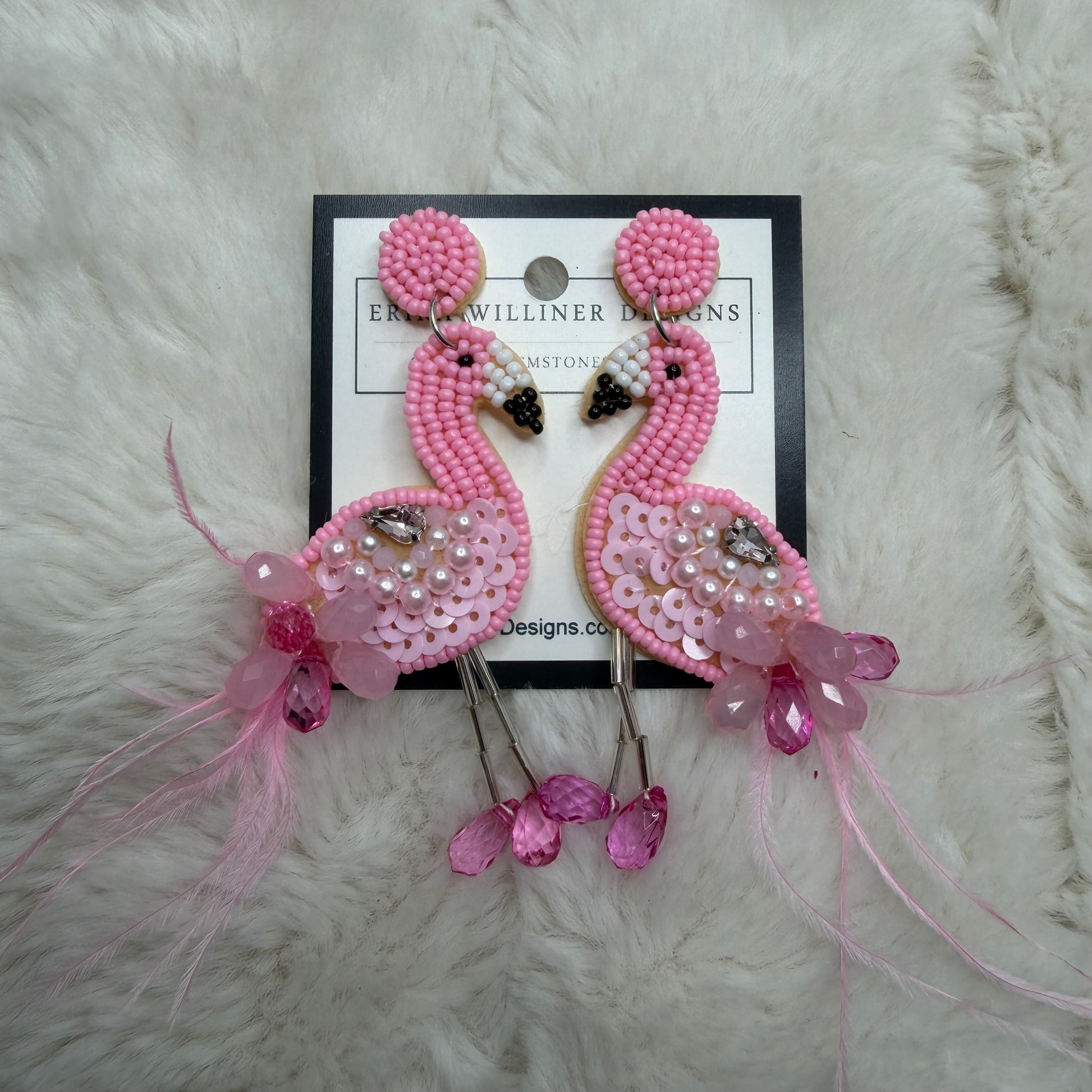 Pink beaded earrings on a branded card against a white fur background